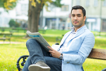 Obraz premium Young businessman sitting on bench and reading newspaper