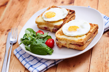 Croque monsieur with eggs and salad on vintage table wide