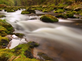 Obraz premium Noisy stream with blurred waves, water run over boulders