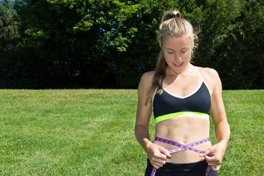 Fit woman measuring her weight loss with a measuring tape