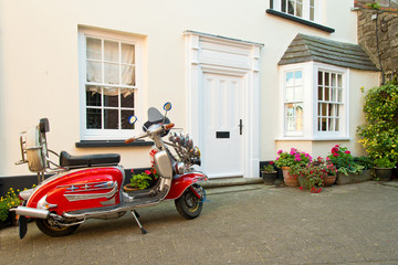 Red vintage scooter parked in front of english house