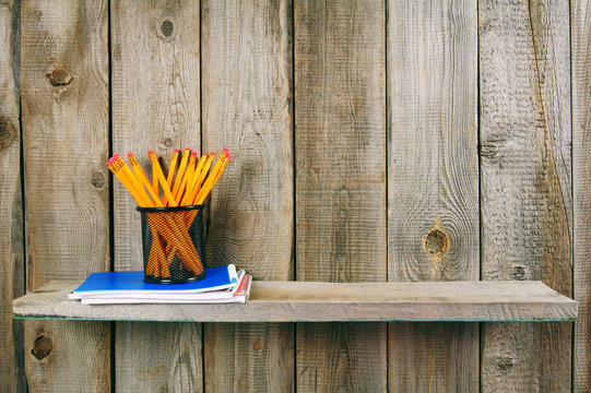 Pencils and writing-books on a wooden shelf.