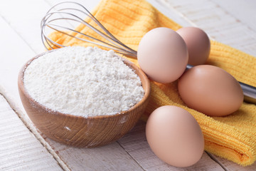 Fototapeta na wymiar Flour in wooden bowl, eggs on table.