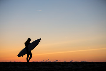 silhouetted girl with surfboard in sunset at beach
