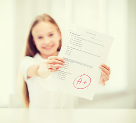 smiling little student girl with test and A grade