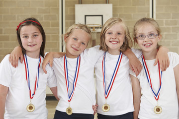 Female School Sports Team In Gym With Medals