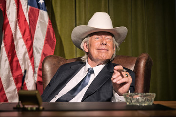 Big boss with white cowboy hat smoking cigar sitting behind desk