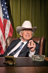 Big boss with white cowboy hat smoking cigar sitting behind desk