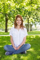 Obraz premium Pretty redhead smiling at camera in the park