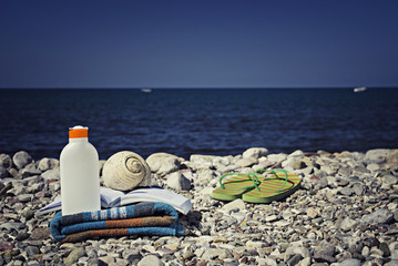 Sunscreen Bottle on Towel with seashell, book and flip flopps on
