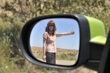 Woman hitchhiking reflected in the rearview mirror