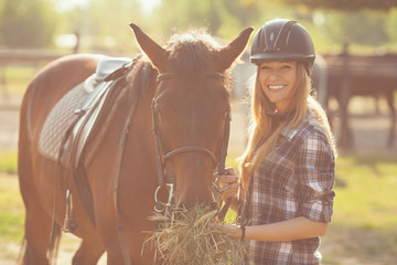 Beautiful young woman feeding her horse with hay