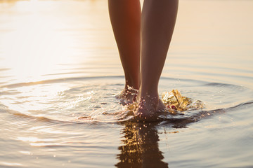 Woman walking in the shallow water at sunset