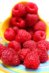 Fresh raspberries pouring out of yellow bowl