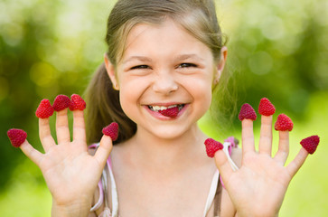 Young girl is holding raspberries on her fingers