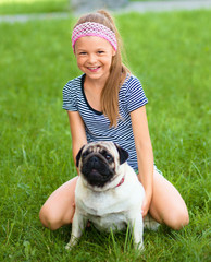 Little girl and her pug dog on green grass