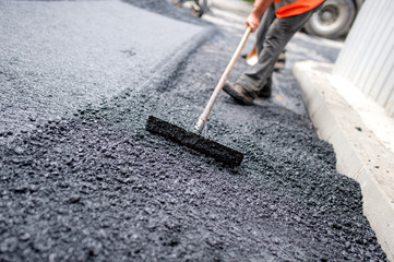 Worker leveling fresh asphalt on a road building - obrazy, fototapety, plakaty