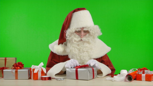 Santa Claus is Wrapping a Gift with Silver Colored Paper