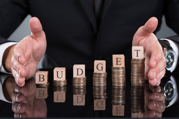 Businessman Protecting Budget Blocks On Stacked Coins