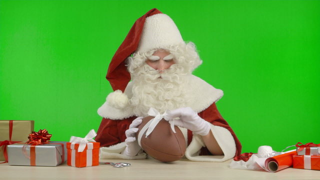 Santa Claus is Tying a Bow on a Football