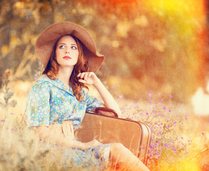 Redhead girl with suitcase sitting at autumn grass