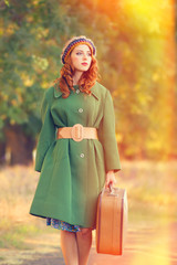 Redhead girl with suitcase at tree's alley.