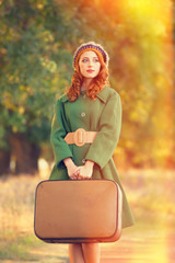 Redhead girl with suitcase at tree's alley.