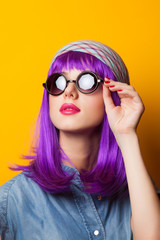 Beautiful girl with violet hair in sunglasses on yellow backgrou