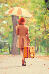 Redhead girl with umbrella and suitcase in the autumn park.