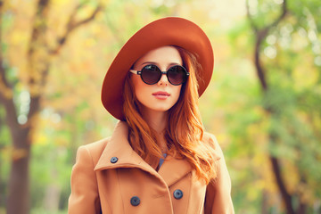 Redhead girl in sunglasses and hat in the autumn park.