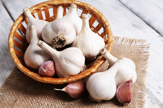 Fresh garlic in wicker basket, on wooden background