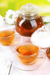 Teapot and cups of tea on table on bright background