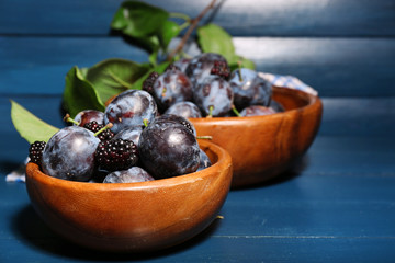 Ripe sweet plums in bowls, on wooden table