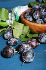 Ripe sweet plums in bowl, on wooden table