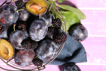 Ripe sweet plums in old metal basket, on pink wooden table