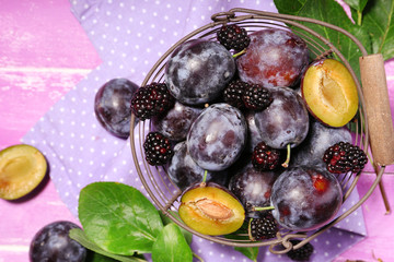 Ripe sweet plums in old metal basket, on pink wooden table