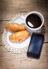 A cup of coffee with croissants and smartphone