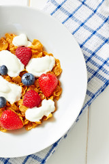 Corn flakes with yogurt and berries on white plate top cropped