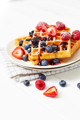 Golden waffles with berries on white table close up