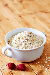 Raw oatmeal and raspberries on a wooden table wide view