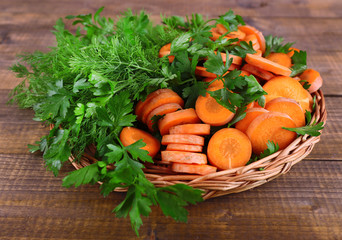 Slices of carrot and parsley in wicker bowl on wooden