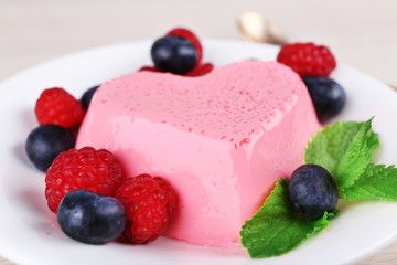 Heart shaped cake with berries on plate on wooden background