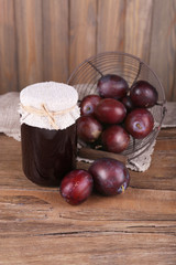 Tasty plum jam in jar and plums on wooden table close-up