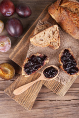 Bread with plum jam and plums on wooden table close-up