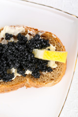 Slice of bread with butter, black caviar and lemon