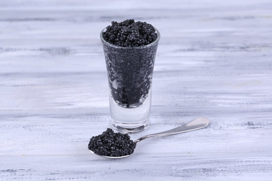 Glass and spoon of black caviar on grey wooden background