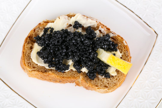 Slice of bread with butter, black caviar and lemon