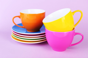 Colorful cups and saucers on color background