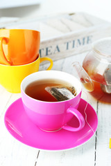 Cup with tea, teapot and tea bags on wooden table close-up
