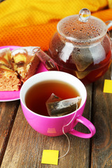 Cup with tea, teapot and tea bags on wooden table close-up